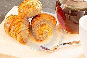 Fresh croissants, spoon and honey jar over wooden board, breakfast, selective focus and close-up