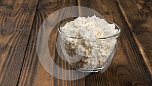 Fresh crumbly cottage cheese in a glass bowl on a wooden table