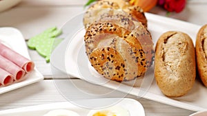 Fresh crusty loaves of bread and bun with ham, eggs, radish on white table in 4K VIDEO.