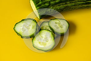 Fresh cucumber and slices, closeup, top view, yellow background. photo