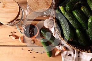 Fresh cucumbers and other ingredients near jars prepared for canning on wooden table, flat lay