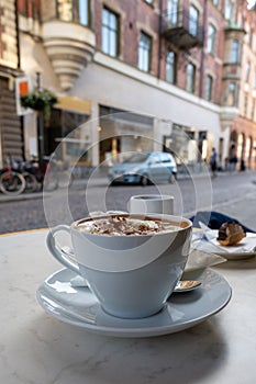 A fresh cup of hot chocolate of coffee in a white cup with saucer on streetside cafe table photo