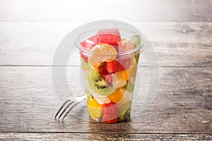 Fresh cut fruit in a plastic cup on wood