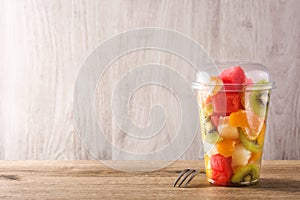Fresh cut fruit in a plastic cup on wood