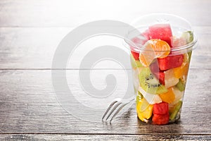 Fresh cut fruit in a plastic cup on wood