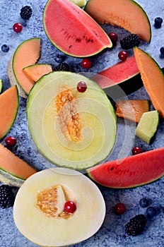 Fresh cut melons, watermelon and berries on a blue stone background