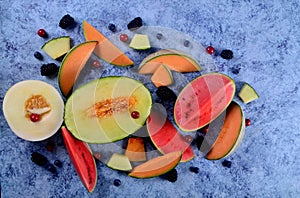 Fresh cut melons, watermelon and berries on a blue stone background