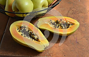 Fresh cut papaya halves with black seeds, apples wire basket