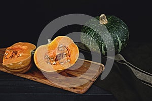 Fresh cut pumpkin with seeds on wooden board with black background