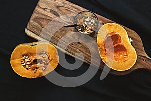 Fresh cut pumpkin with seeds on wooden board with black background