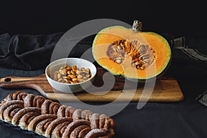 Fresh cut pumpkin on wooden board with cinnamon roll bread on black background