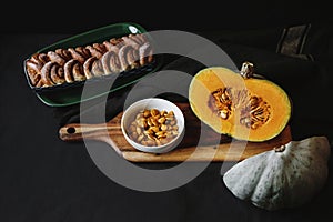 Fresh cut pumpkin on wooden board with cinnamon roll bread on black background