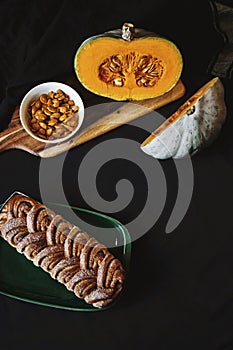 Fresh cut pumpkin on wooden board with cinnamon roll bread on black background