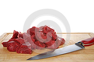 Fresh cut stew meat on a wood cutting board with knife