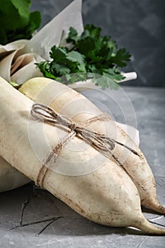 Fresh daikon radish on a gray background, against a background of bunches of greenery, large pla. Rustic gray wooden