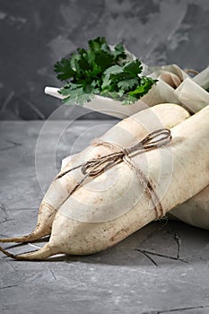 Fresh daikon radish on a gray background, against a background of bunches of greenery, large pla. Rustic gray wooden