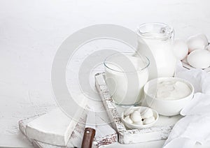 Fresh dairy products in vintage wooden box on white table background. Jar and glass of milk, bowl of sour cream and cheese. Space