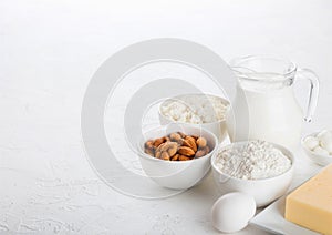 Fresh dairy products on white table background. Glass jar of milk, bowl of cottage cheese and baking flour and almond nuts. Eggs a