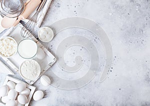 Fresh dairy products on white table background. Glass of milk, bowl of flour and cottage cheese and eggs. Box of baking utensils.