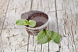 Fresh dark chocolate muffin with mint leaves on rustic wooden table