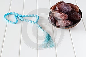 Fresh dates Medjool in wooden coconut bowl and blue rosary.