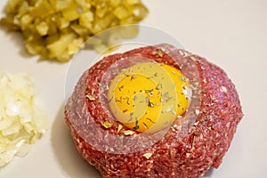 Fresh delicious beef tartare served with a raw egg, cut onions and pickles, raw meat dish macro, extreme closeup, tatar meal