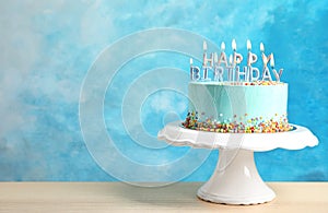 Fresh delicious birthday cake with candles on stand against color background.