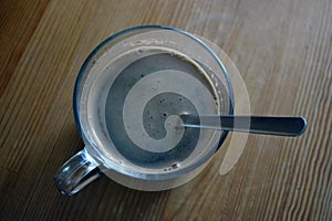 Fresh delicious black brewed coffee is poured into a glass cup and placed on a wooden table.