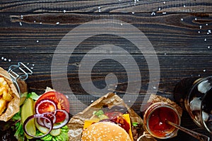 Fresh delicious burgers with french fries, sauce and drink on the wooden table top view, with copy space