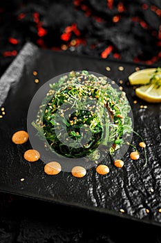 Fresh delicious Chukka seaweed Wakame salad ina black plate on a black stone background with limon and sauce