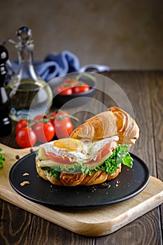 Fresh and delicious Croassan sandwich with green salad, tomatoes, cheese and scrambled eggs on a wooden board and a