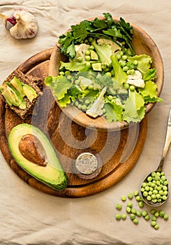 Fresh delicious green salad with avocado in a wooden plate and gluten free toast. Top view. Healthy lunch dish and Diet detox food