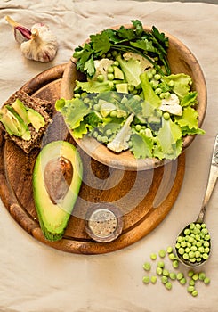 Fresh delicious green salad with avocado in a wooden plate and gluten free toast. Top view. Healthy lunch dish and Diet detox food