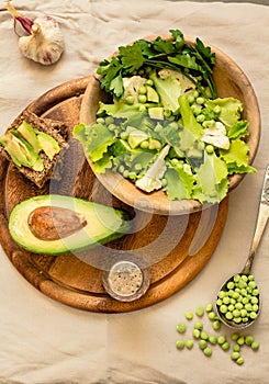 Fresh delicious green salad with avocado in a wooden plate and gluten free toast. Top view. Healthy lunch dish and Diet detox food