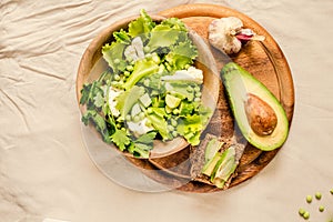 Fresh delicious green salad with avocado in a wooden plate and gluten free toast. Top view. Healthy lunch dish and Diet detox food