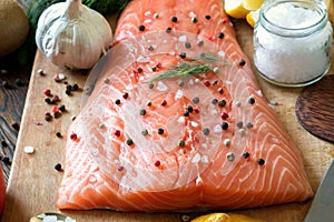 Fresh delicious salmon fillet with aromatic herbs, spices, garlic, lemon on dark background. Top view. Closeup.