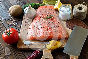 Fresh delicious salmon fillet with aromatic herbs, spices, garlic, lemon on dark background. Top view. Closeup.