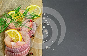 Fresh dogfish fillets with herbs and lemon on black background