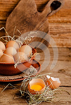 Fresh domestic eggs and broken eggshell with yolk on rustic wooden background