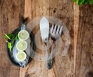 Fresh dorada fish decorated with lemon, peppers and bay leaf on metal plate with silverware