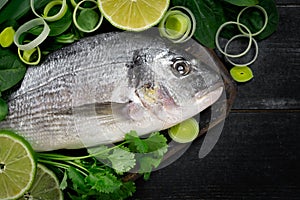 Fresh dorada fish with herbal, onion, parsley and lime on a cutting board on black background