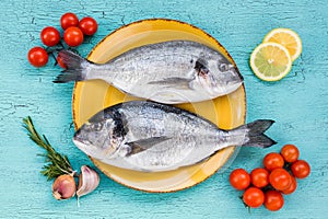 Fresh dorado fish on yellow plate and vegetables on blue background.