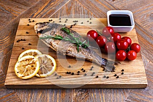 Fresh dorado grill with lemon and cherry tomatoes on a wooden tray. For restaurant menu or recipe