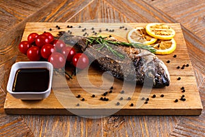Fresh dorado grill with lemon and cherry tomatoes on a wooden tray. For restaurant menu or recipe