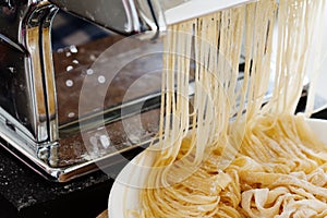 Fresh dough for pasta and pasta machine on kitchen table with in