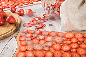 Fresh and dried strawberries from dehydrator for long term prepper pantry with knife, wooden cutting board and glass jar on light