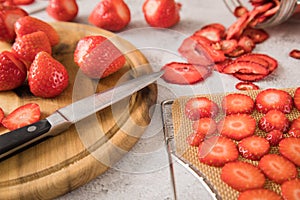 Fresh and dried strawberries from dehydrator for long term prepper pantry with knife, wooden cutting board and glass jar on light