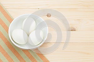 Fresh duck egg in bowl on napery and wood background.