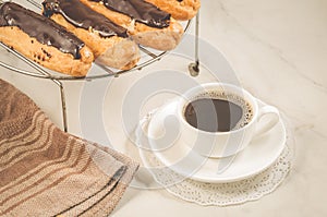 Fresh eclairs with chocolate and a coffee cup/fresh eclairs with