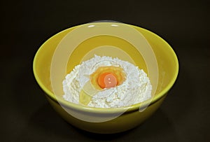 Fresh egg on raw flour in yellow ceramic mixing bowl